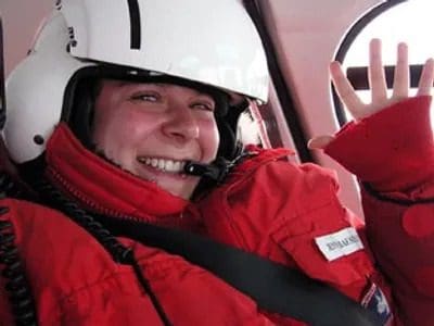 A woman in red jacket and helmet riding on the back of a vehicle.